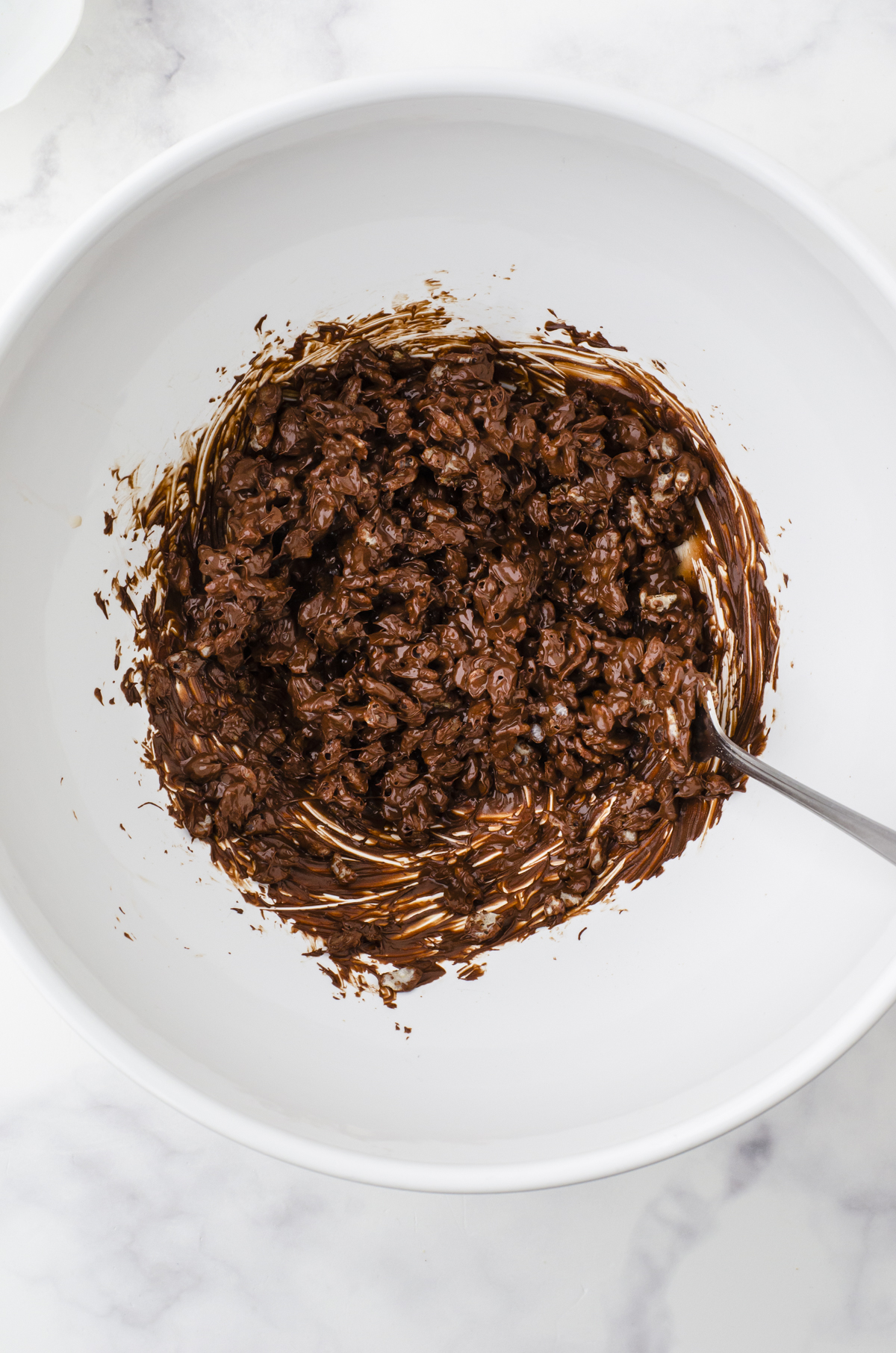 Rice Krispies being stirred into melted chocolate for the top layer of caramel chocolate rice crispies squares.