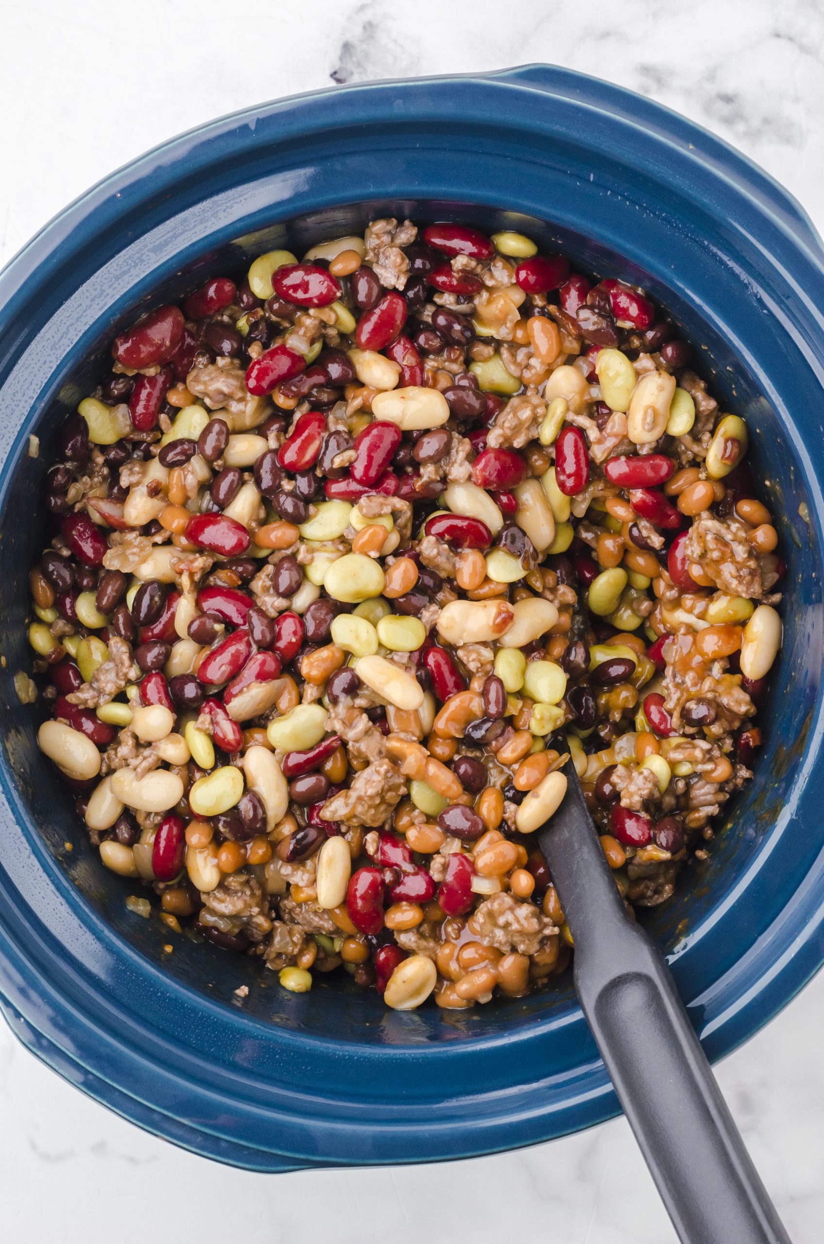 Ingredients for crock pot calico baked beans stirred together in a slow cooker.