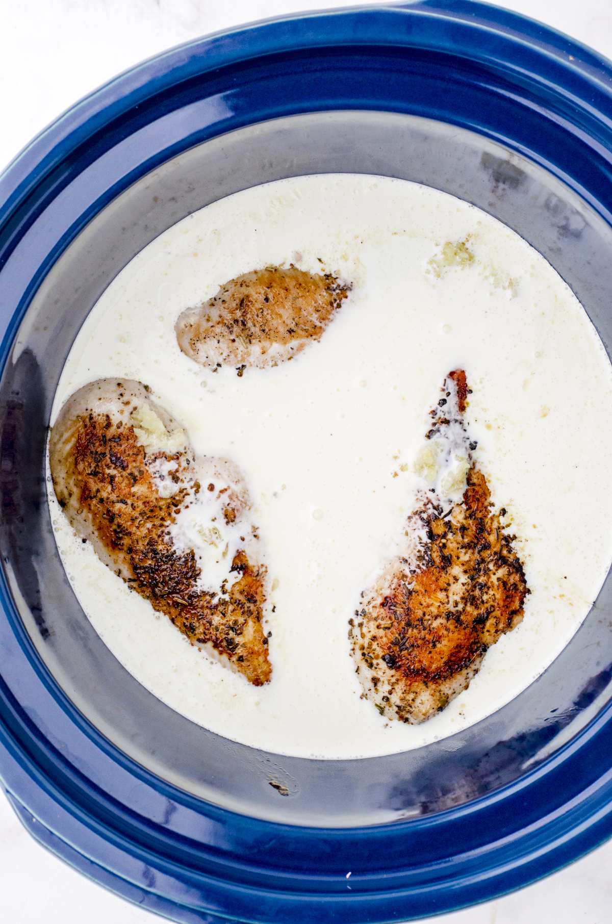Heavy cream on top of the chicken breasts and garlic in a crock pot for slow cooker chicken alfredo recipe.