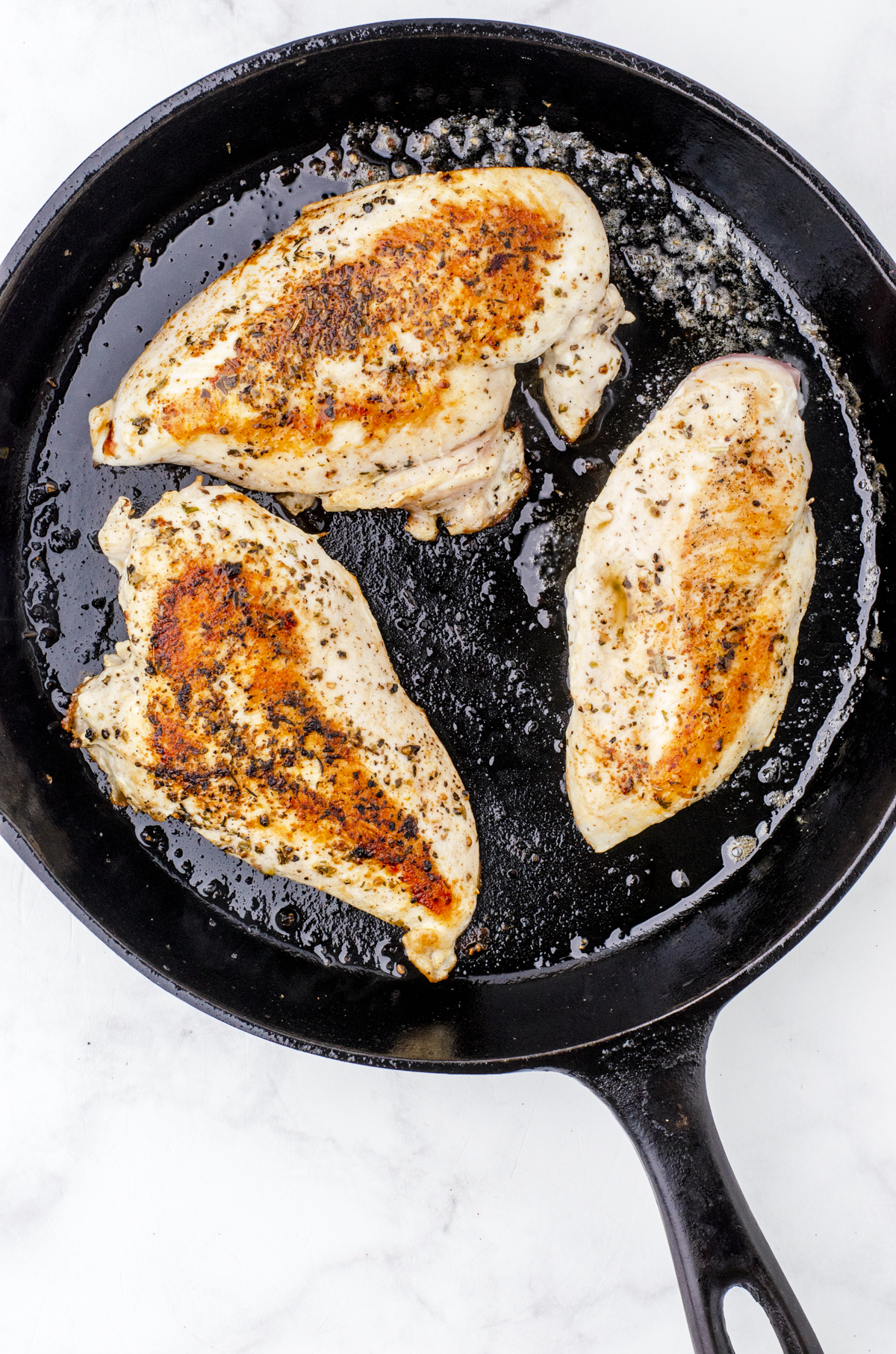 Chicken breasts being seared in a cast iron pan in preparation for being used for alfredo chicken in the crockpot