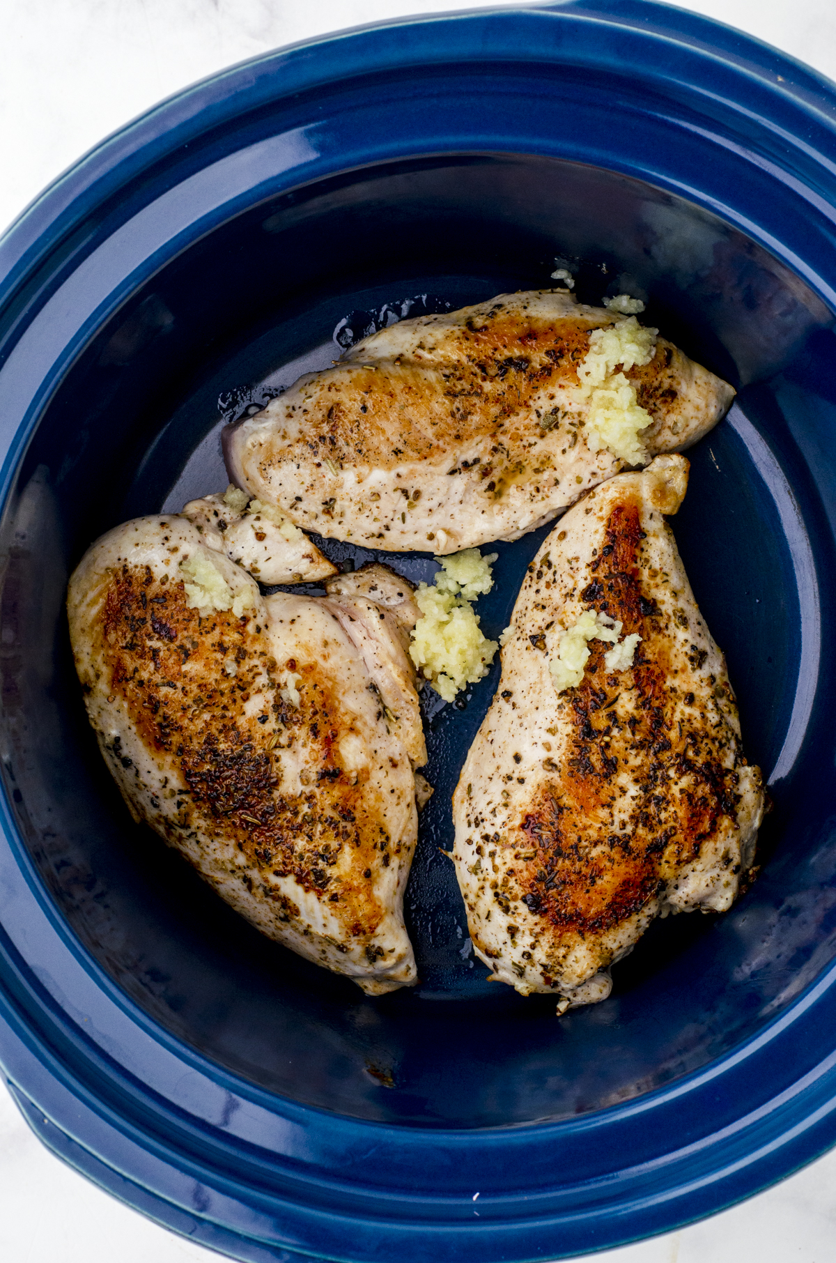 Crushed garlic added to chicken breasts in the bottom of a crock pot in preparation for the chicken alfredo crockpot recipe.