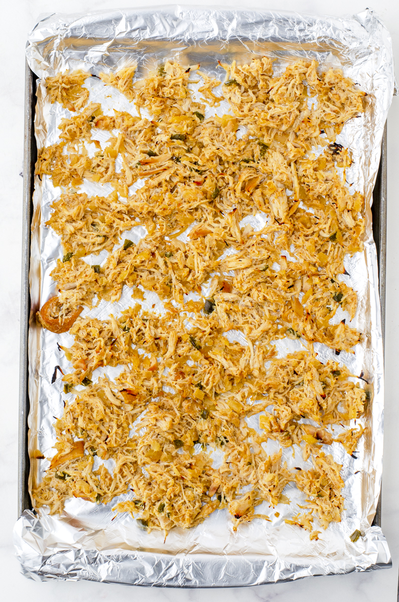 Crock pot shredded chicken on an aluminum foil covered baking sheet