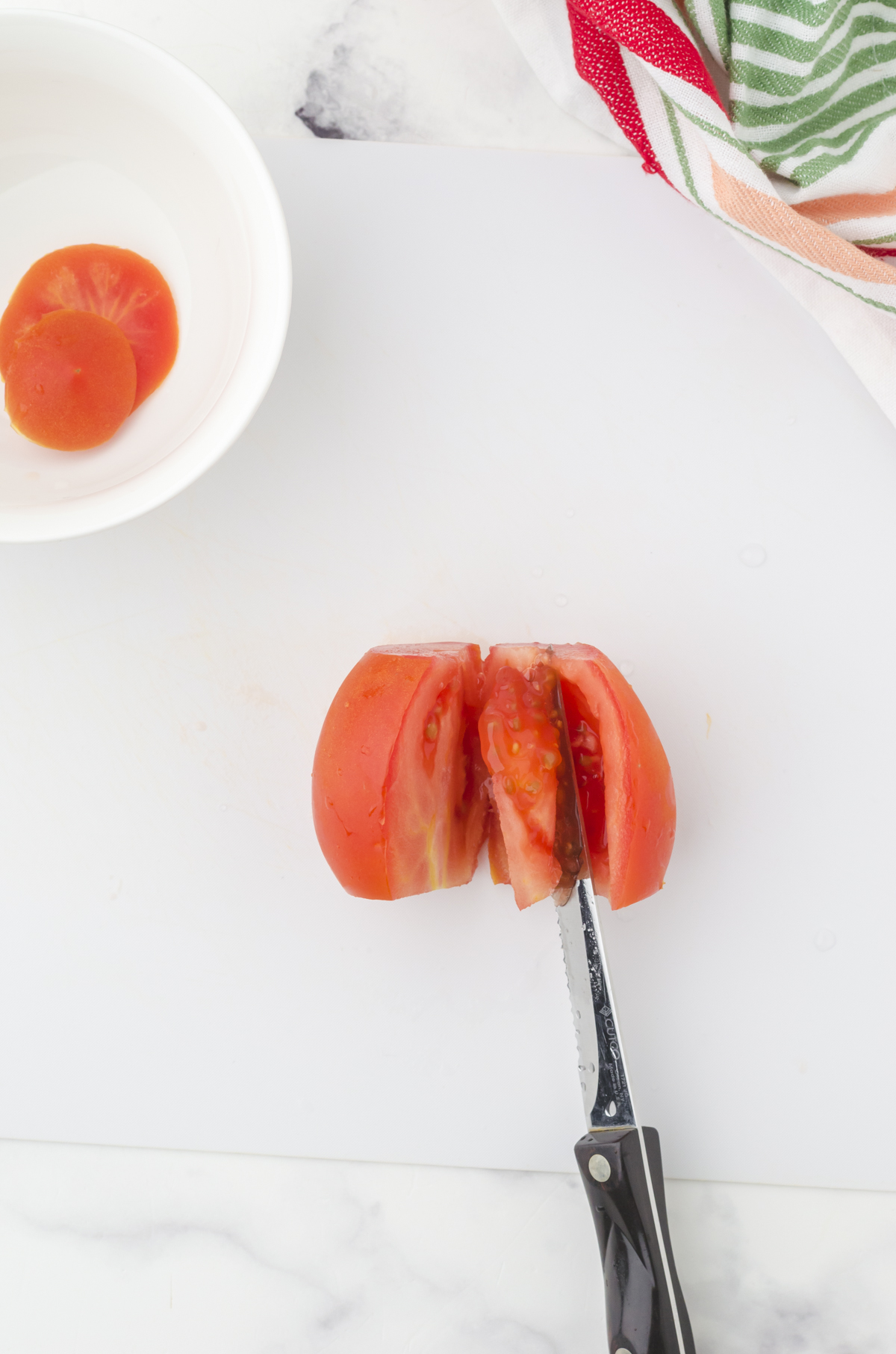 A knife cutting around the inner part of a tomato in order to deseed it.