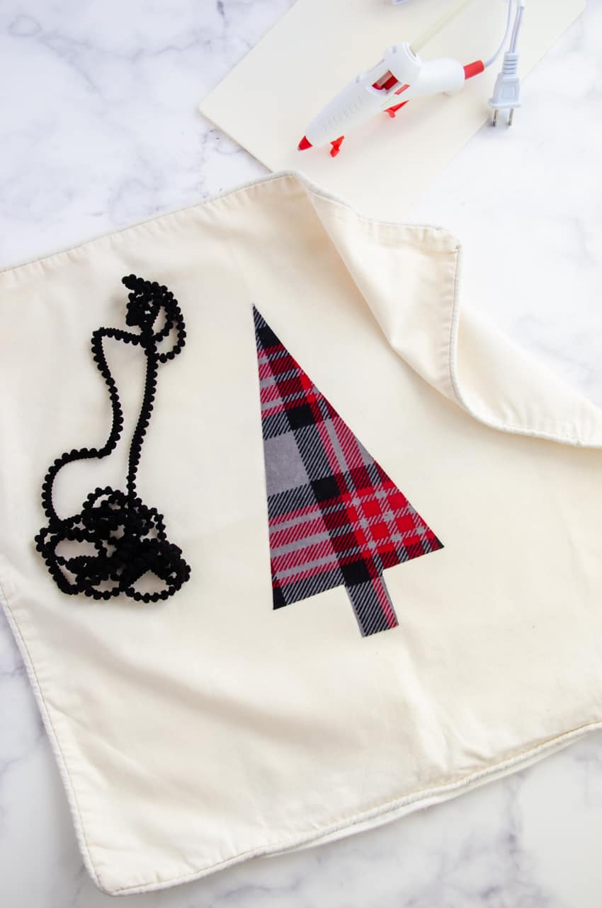 A glue gun can be used to glue on pom pom trim to a DIY Christmas Tree pillow.