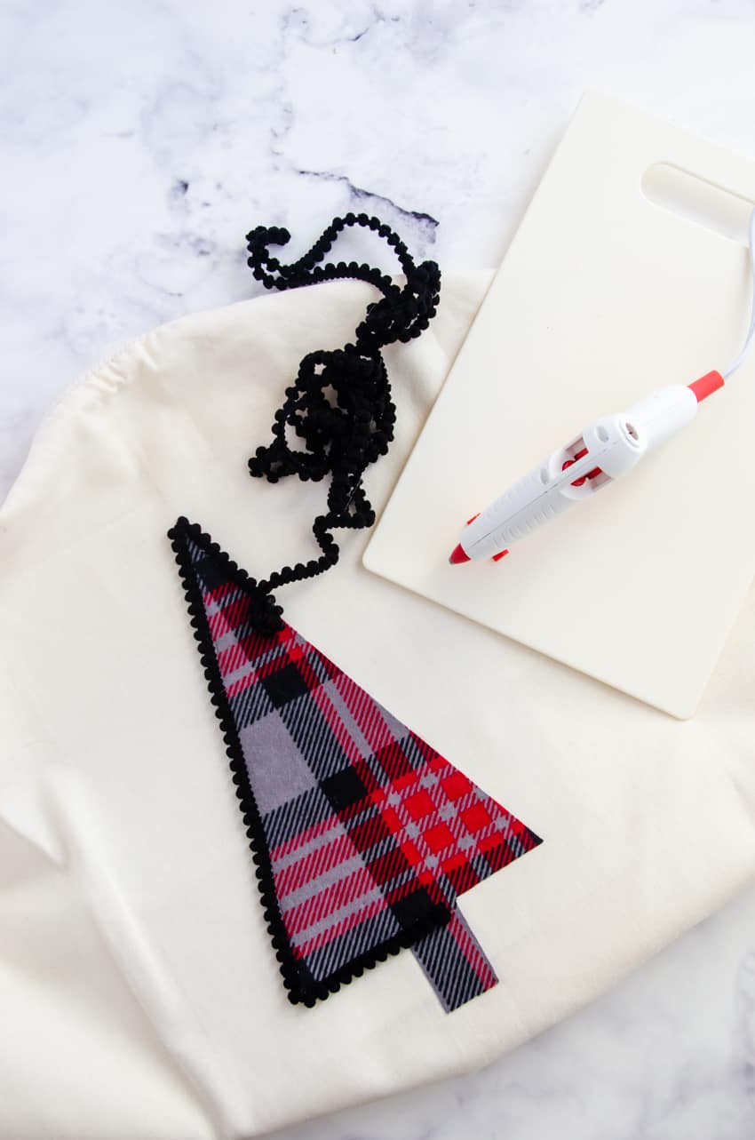 Black pom pom trim around a plaid flannel Christmas tree on a white pillow cover is a great farmhouse style DIY Christmas decor project.