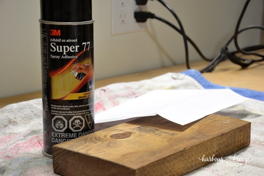Step one of christmas signs diy - spray adhesive onto the board and cover with white cardstock.