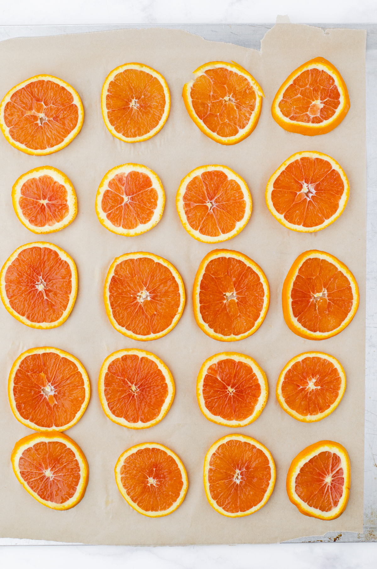 Orange slices laying in a flat layer on a parchment paper lined cookie sheet.