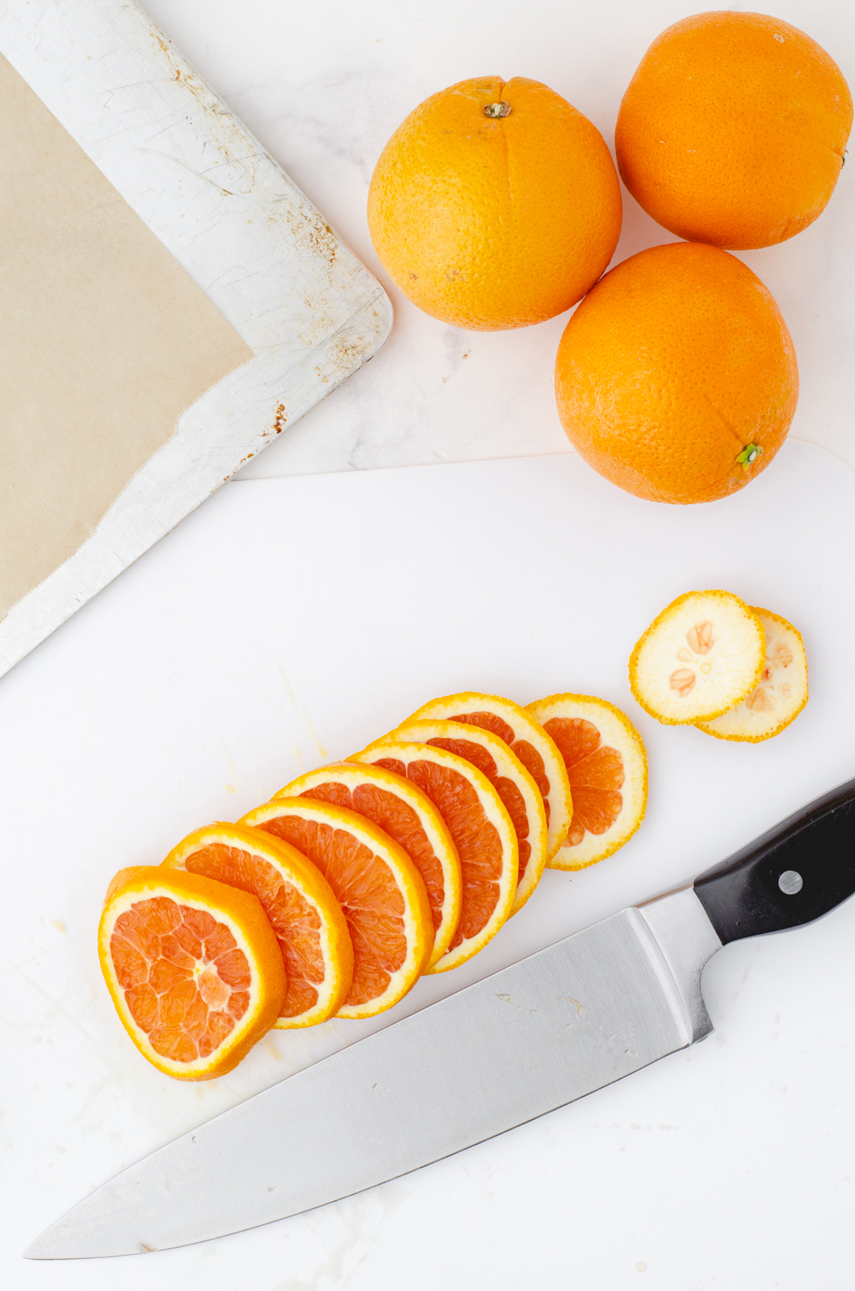 Thin slices of oranges on a cutting board by a knife that will be used to make dried orange slices