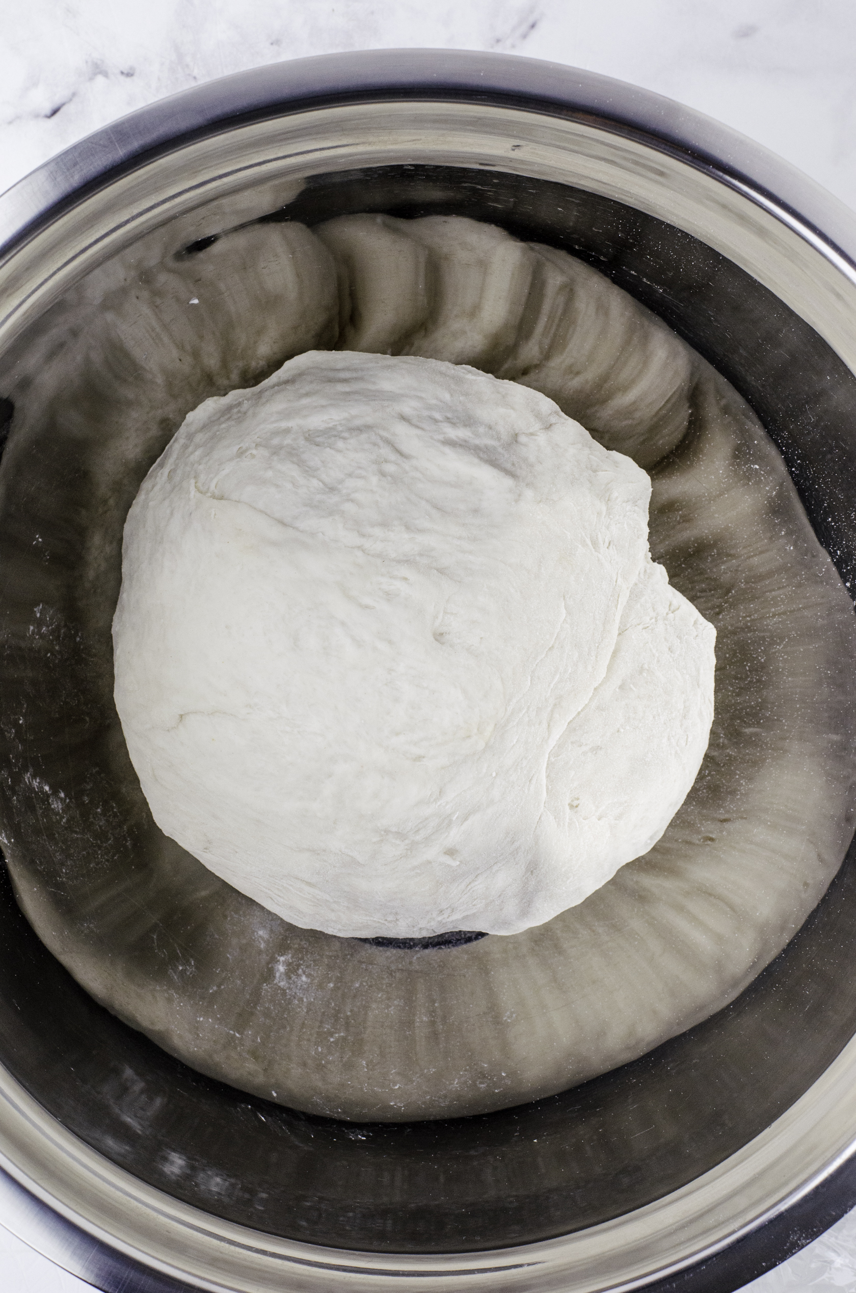 Sourdough bread dough after it has been kneaded slightly and formed into a ball and placed in a large metal bowl to proof.