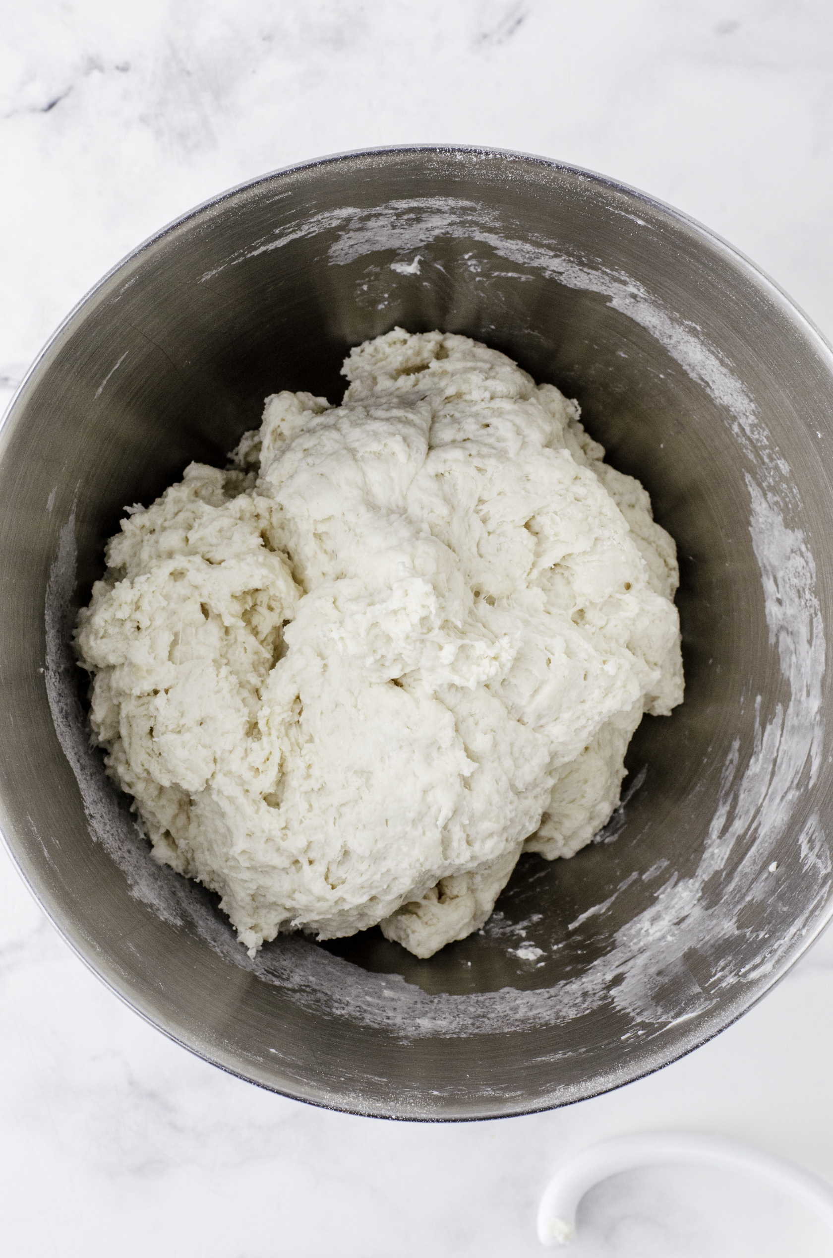 Sourdough bread dough in the mixing bowl of a stand mixer after the flour has been added in and mixed with a dough hook. It isn't super smooth.