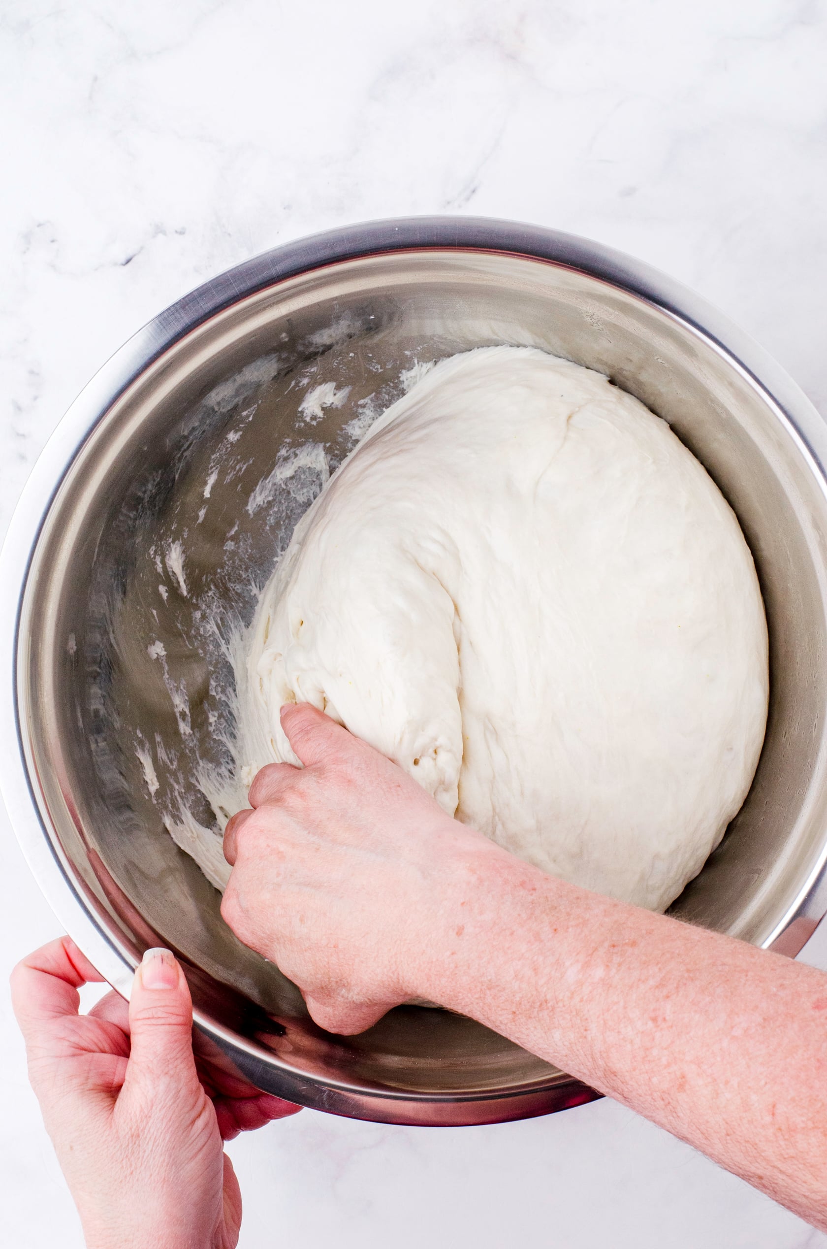 A woman pulling the sourdough dough away from the sides of the bowl.