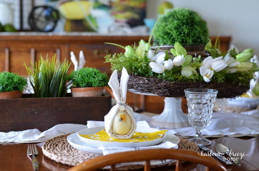 A cloth napkin with the bunny ear napkin fold sitting on top of an easter tablescape setting.