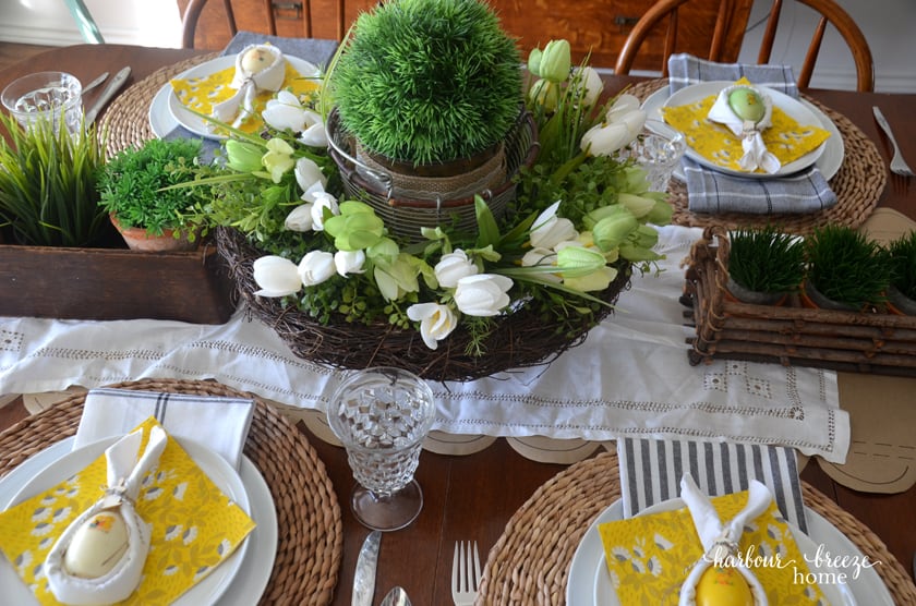 A view from the top of an Easter tablescape featuring bunny ear napkins sitting on yellow floral napkins on the top of white plates.