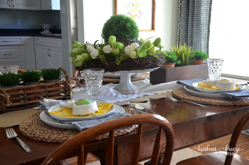 An Easter tablescape featuring bunny ear napkins and faux greenery in the centerpieces of the table.