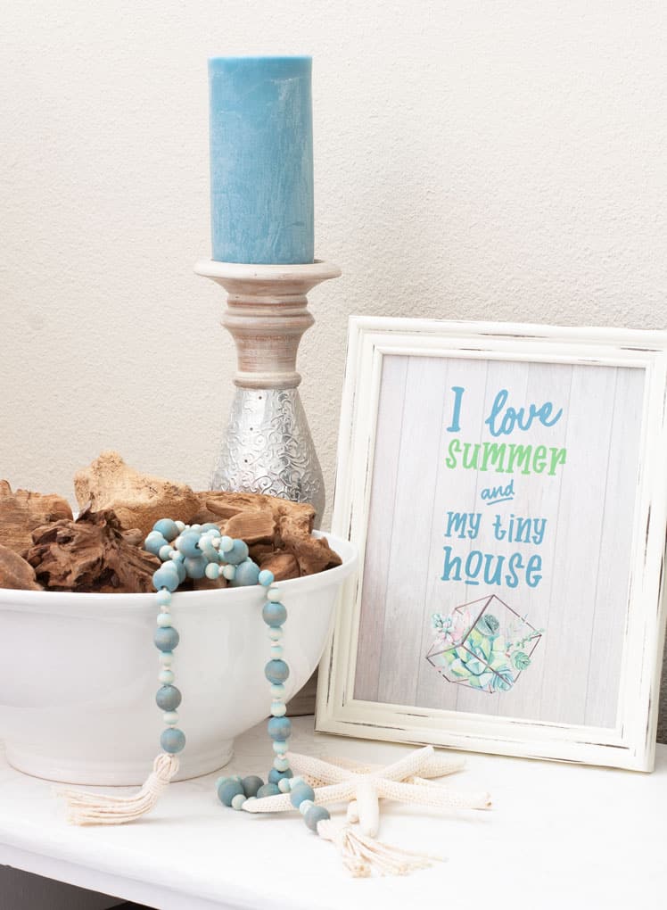 A white bowl filled with small driftwood pieces with a blue bead garland hanging over the edge