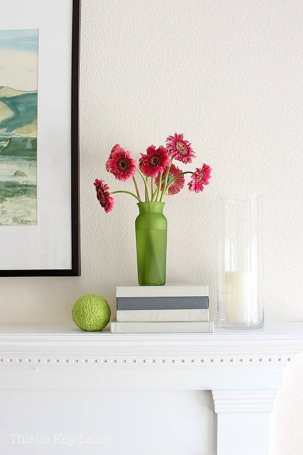Books stacked on a fireplace mantel with a vase of pink flowers sitting on them