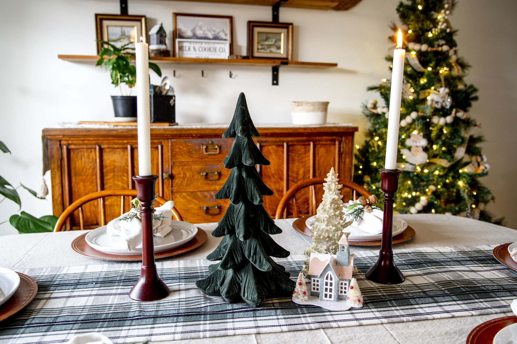 Christmas tablescape centerpiece with taper candles, trees, and a small village house.