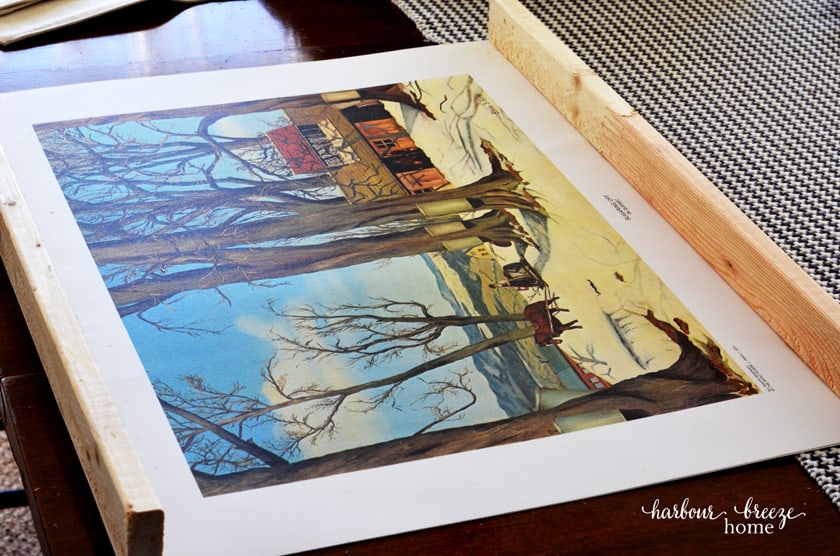 A piece of art work with a wooden rail cut the length of the top and bottom in preparation for making a DIY poster or picture frame.