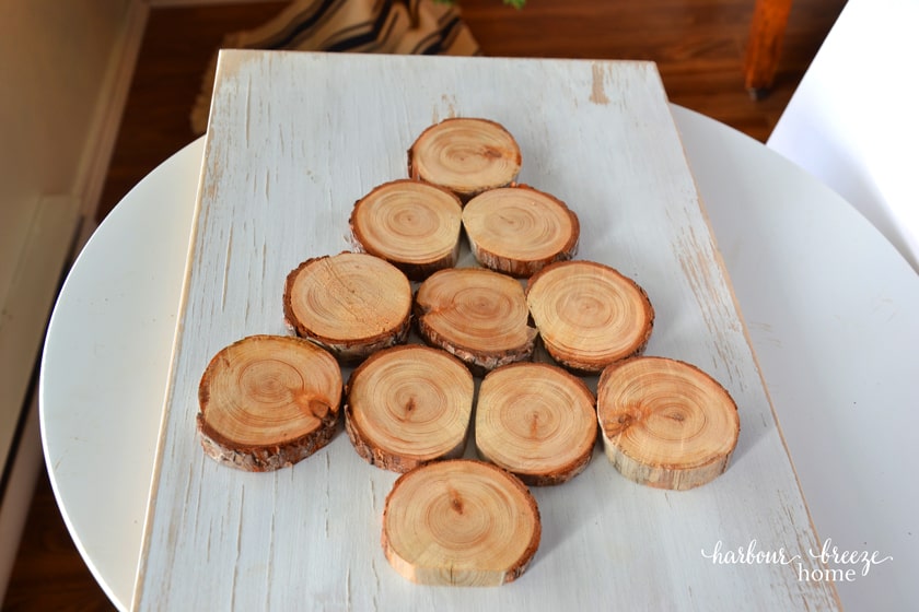 Wood slices arranged on a piece of painted wood to form a Christmas tree shape.