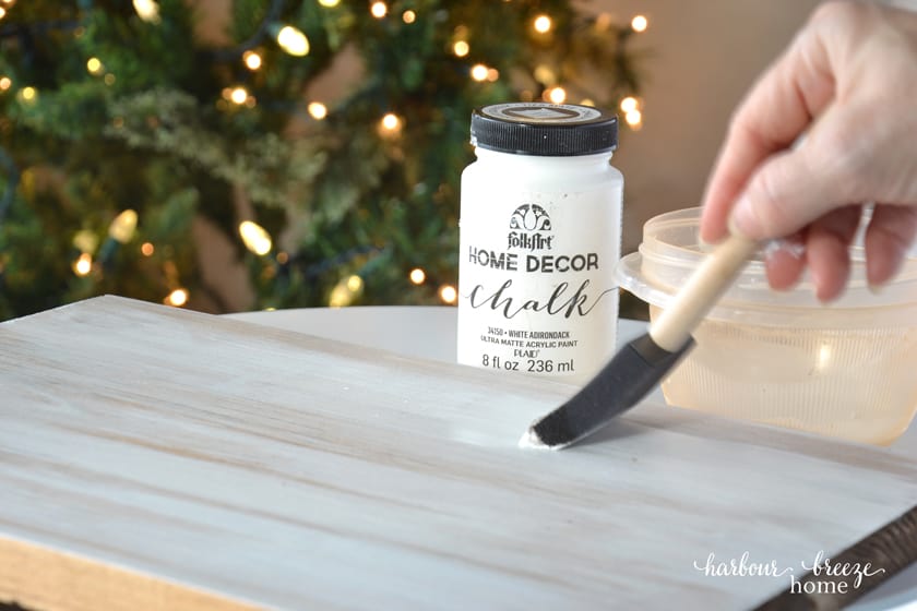 Painting a piece of wood in preparation to make a diy christmas wood sign with a wood slice christmas tree on it.