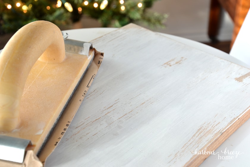 A piece of painted wood being sanded to reveal a hint of wood underneath for an aged and rustic look.