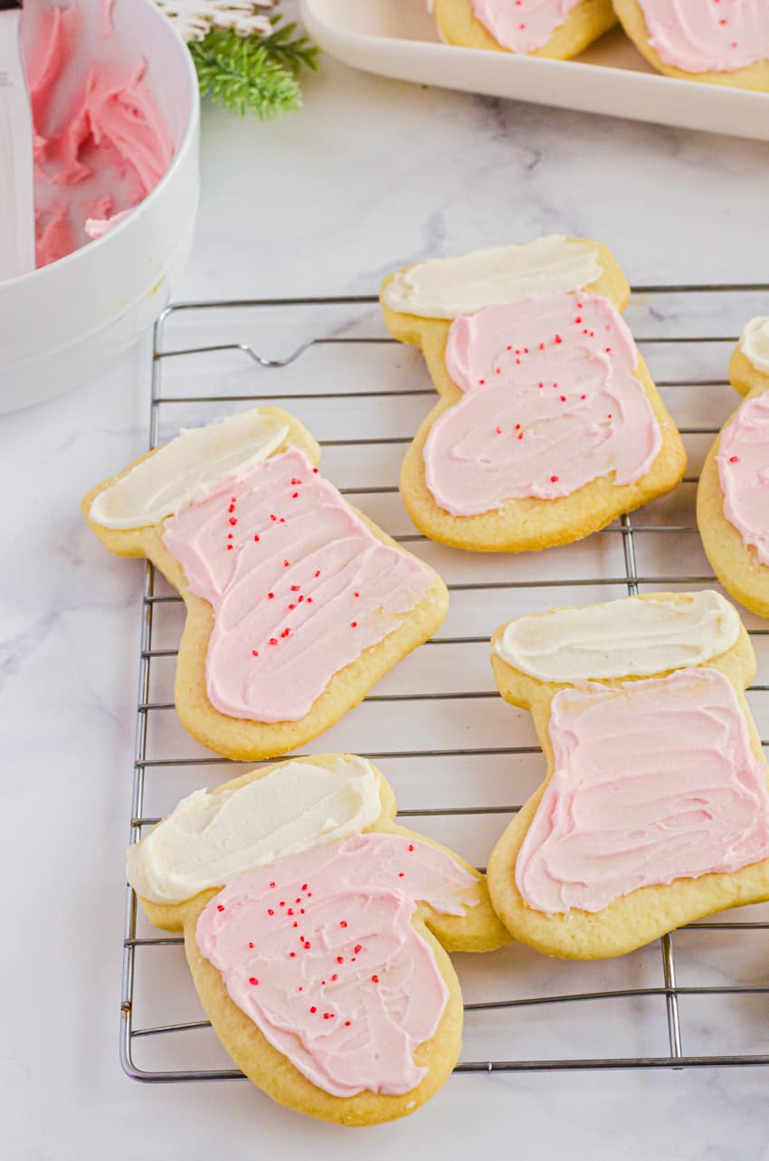 Sugar cookies in the shapes of mittens and stockings spread with easy powdered sugar frosting and sprinkled with decorative sugar.
