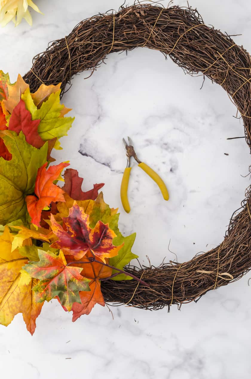 fake leaves being placed into a wreath base for an easy Fall wreath