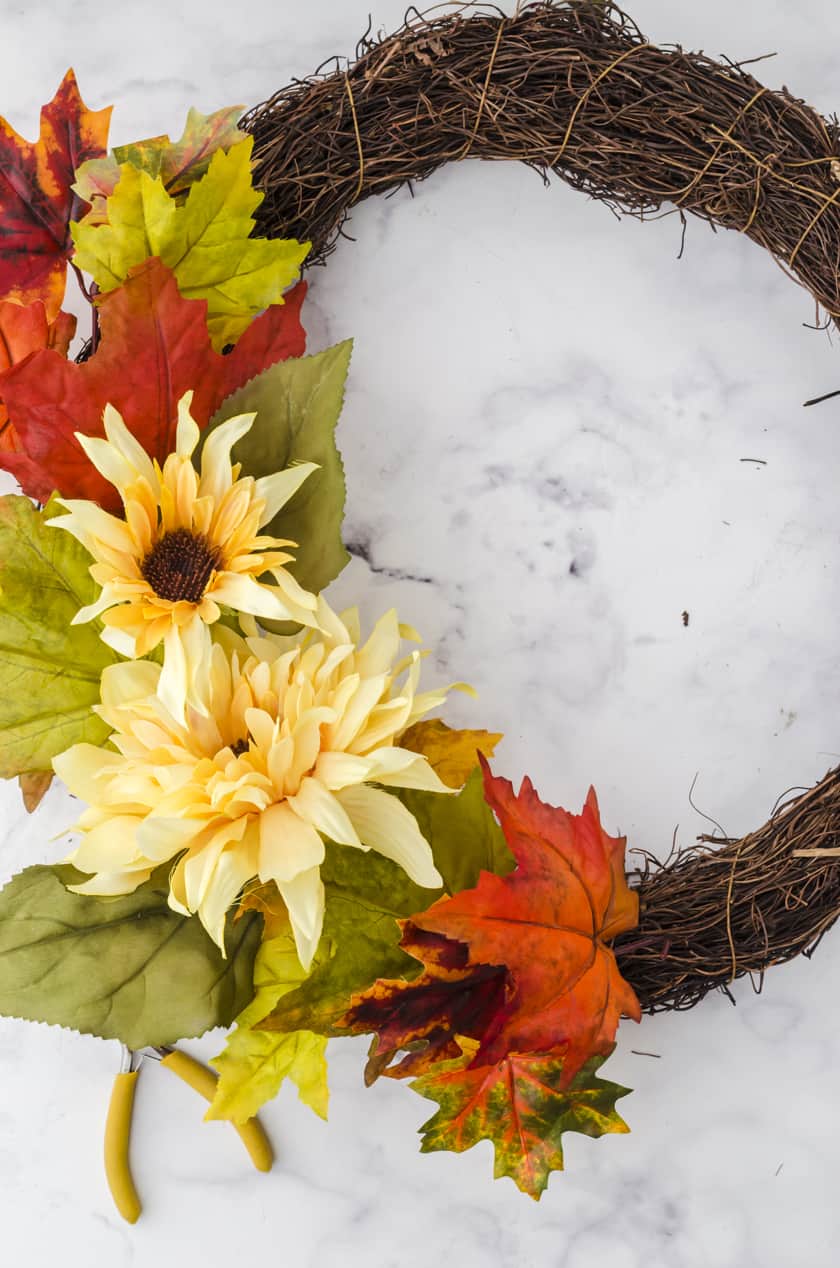 fake flowers and leaves being positioned onto a grapevine wreath base