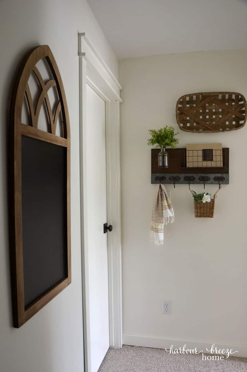 White hallway and trim with farmhouse decor including a chalkboard, metal and wood shelf, a jar of greenery and a basket on the wall