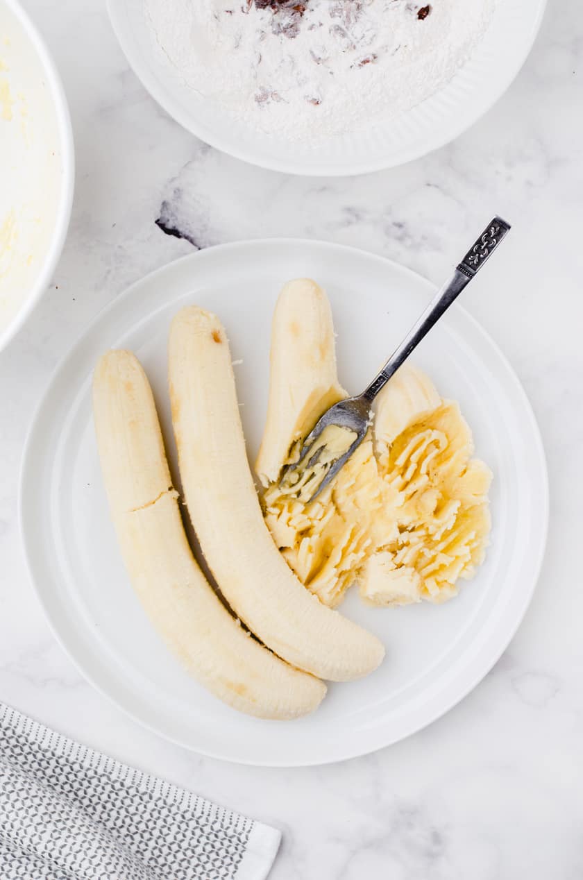 Mash bananas on a plate with a fork.