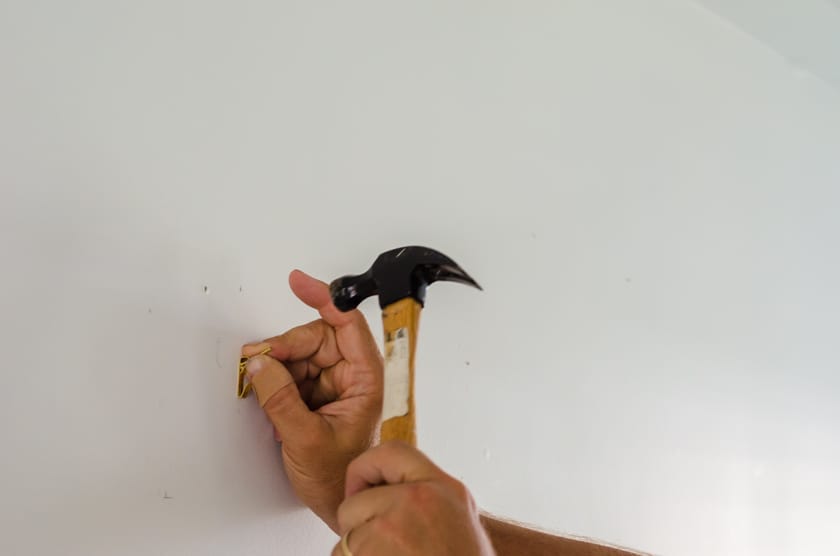 nailing a picture hanger into a drywall wall in preparation for hanging a canvas with floating frame