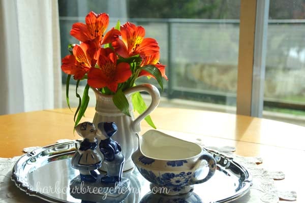 Orange flowers in a vase on a silver platter surrounded by blue print porcelin figurines