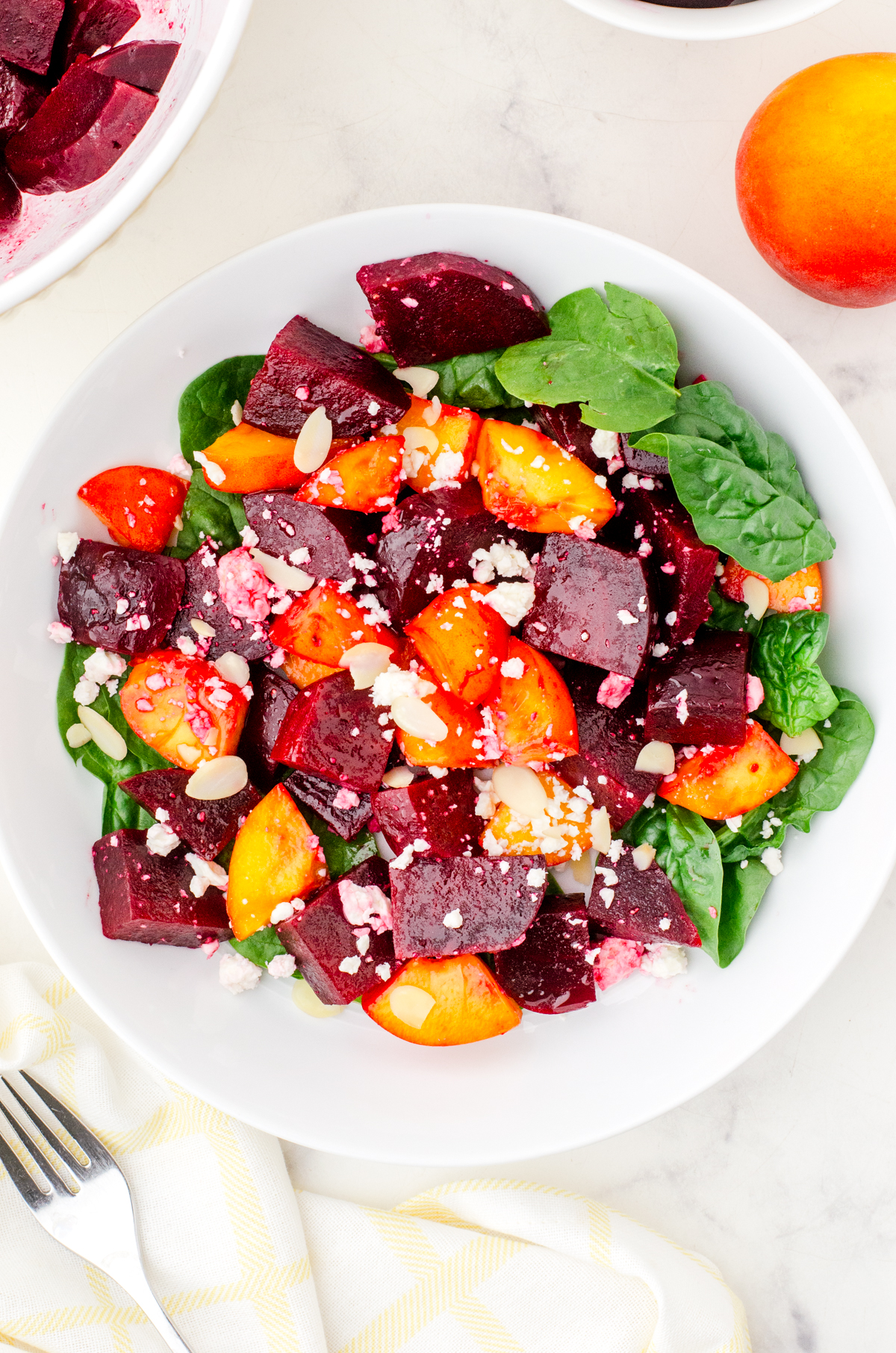 Serving bowl of beet and peach salad on a bed of spinach.