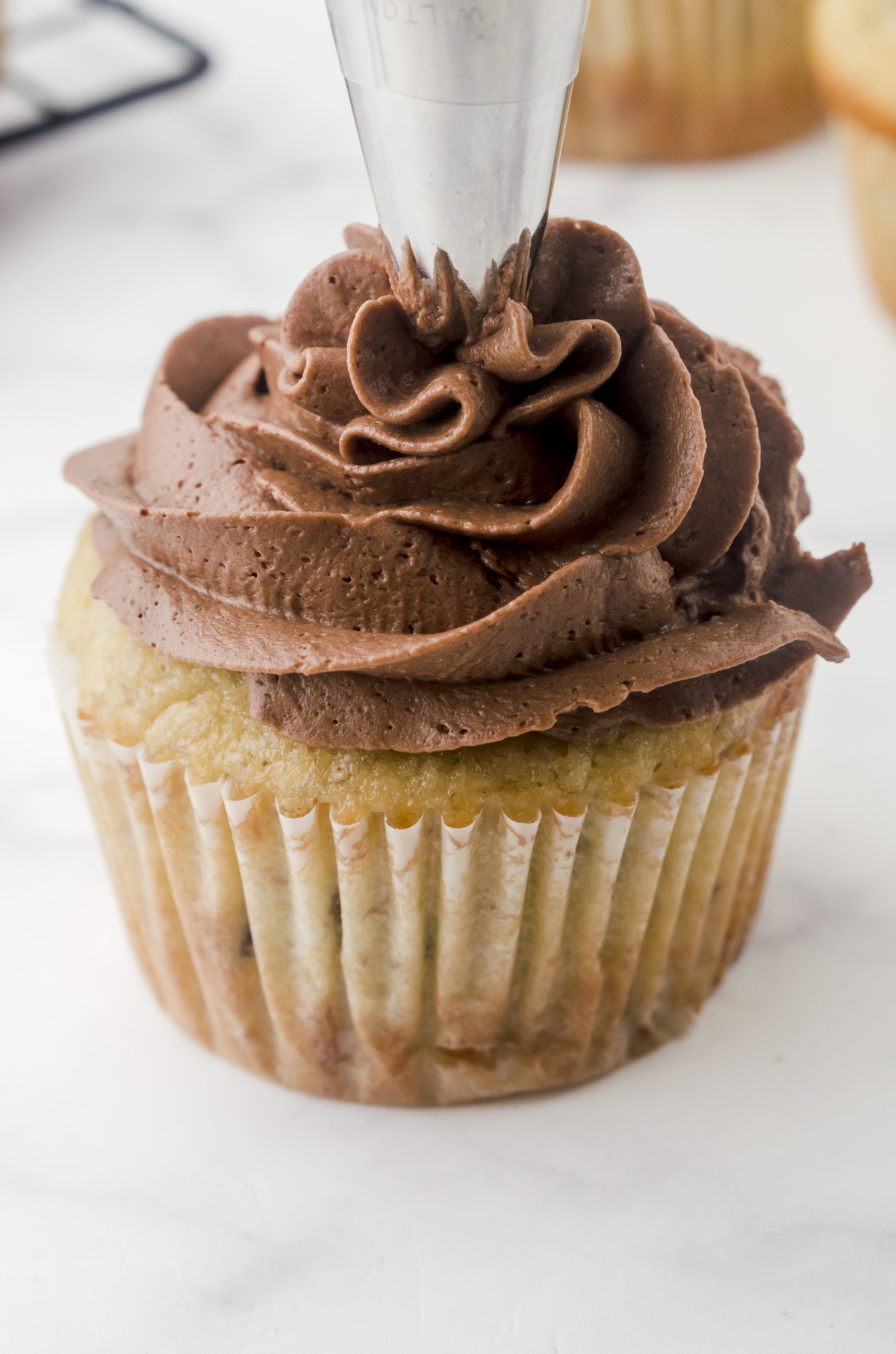 A metal icing tip lifting off the center of a frosted cupcake after it has been piped on.