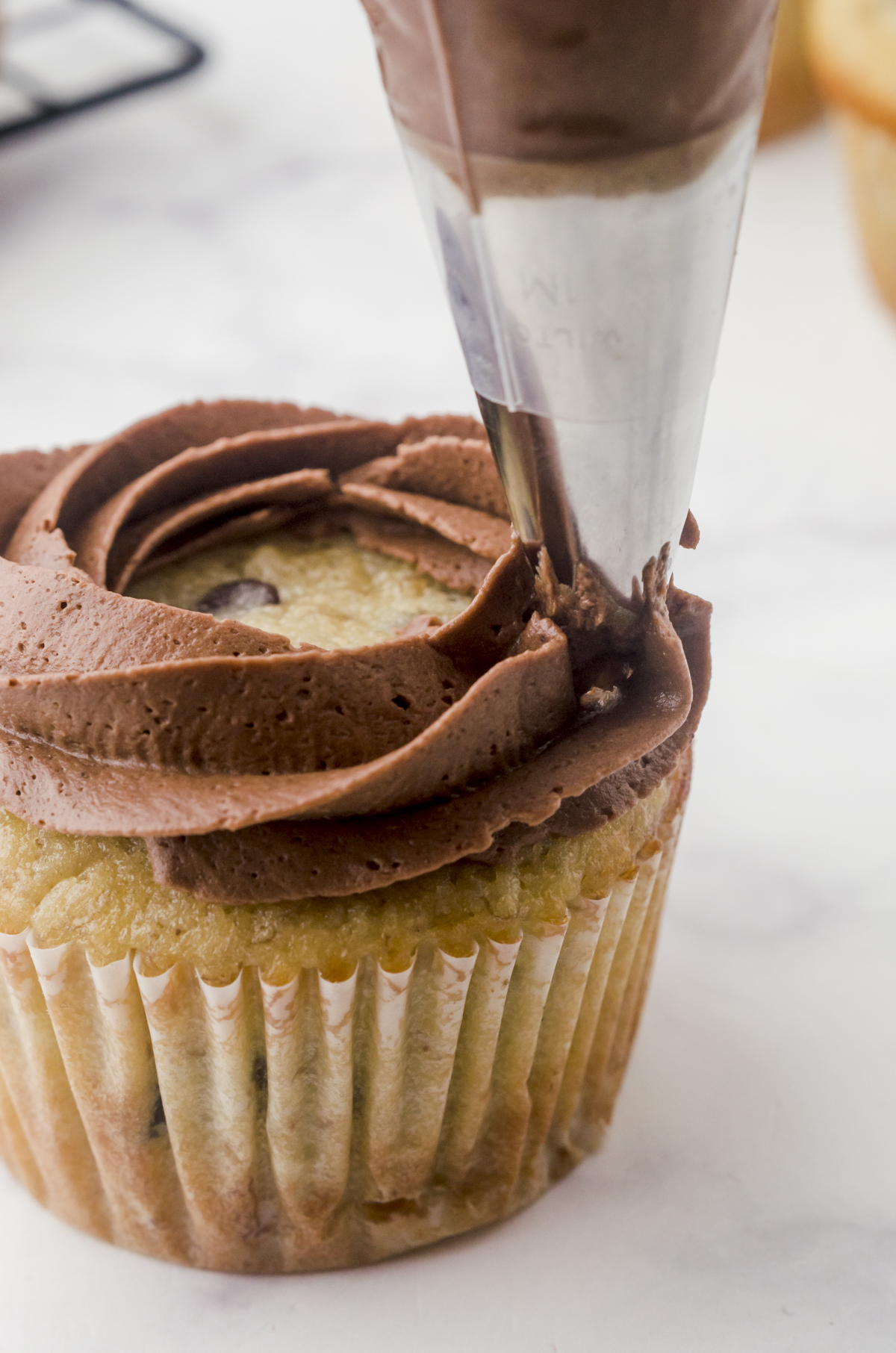 Icing being piped around the outside rim of a cupcake.