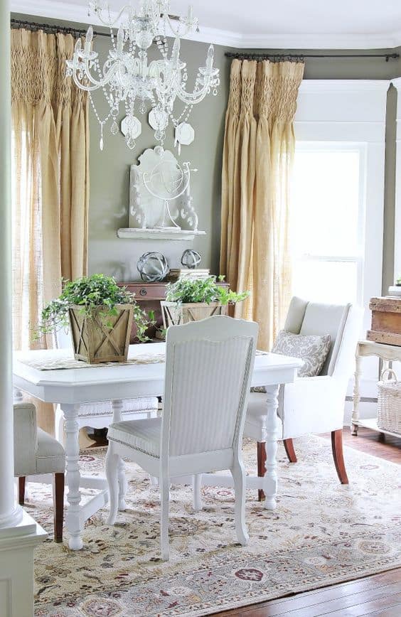 Dining Room with beaded chandelier, burlap curtains, and white table with wood buckets of greenery on it