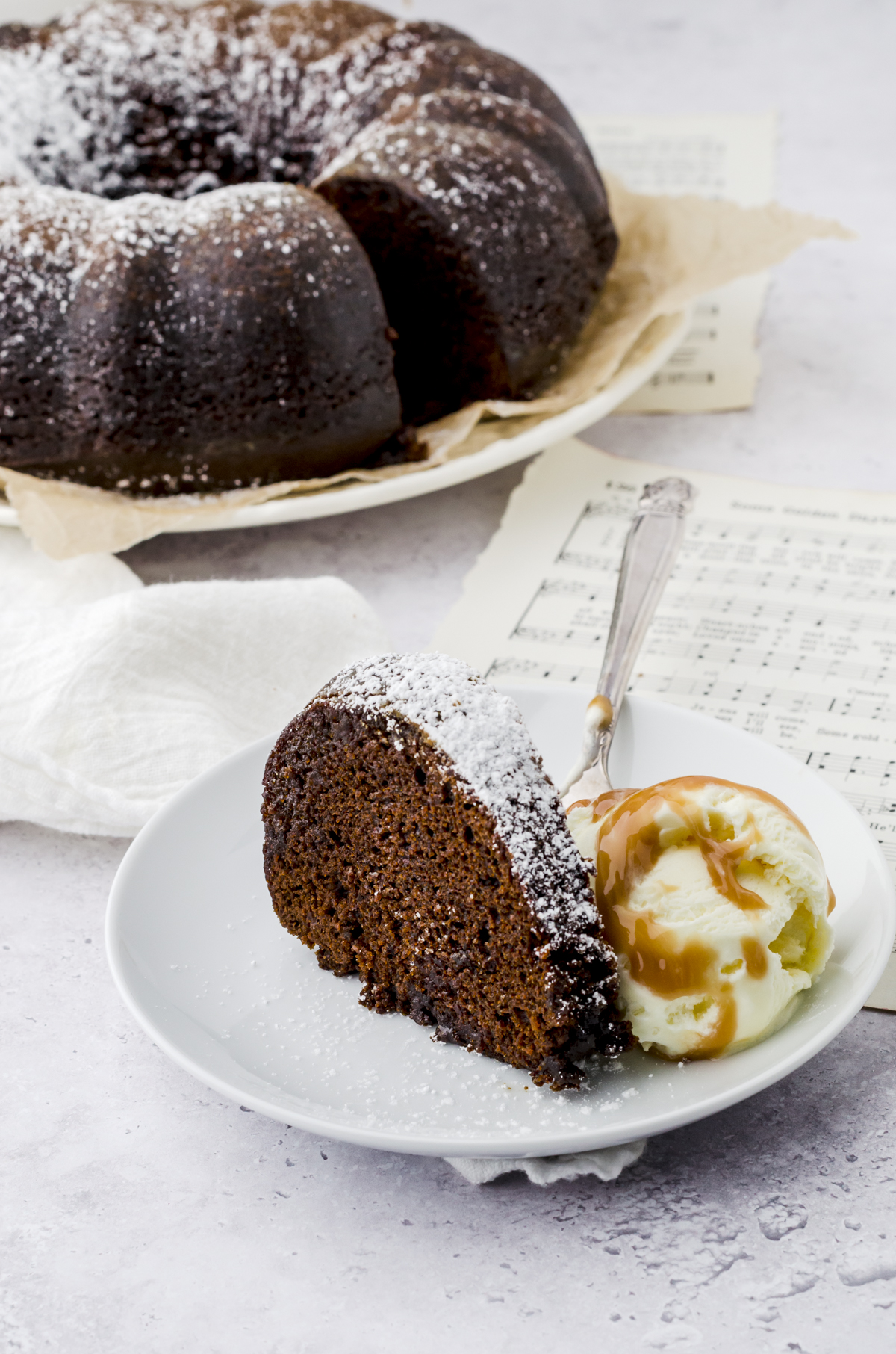 Gingerbread cake in a bundt cake shape sliced on a plate with a scoop of ice cream and caramel sauce on it.