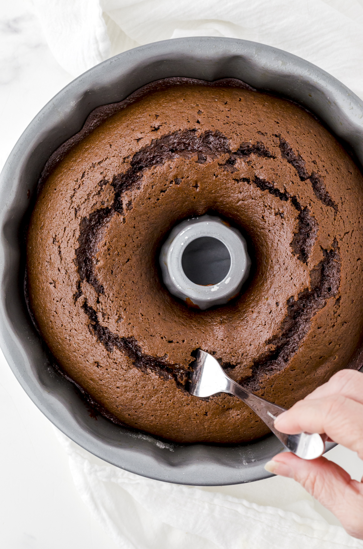 Gingerbread cake baked in a bundt pan being poked with a fork.