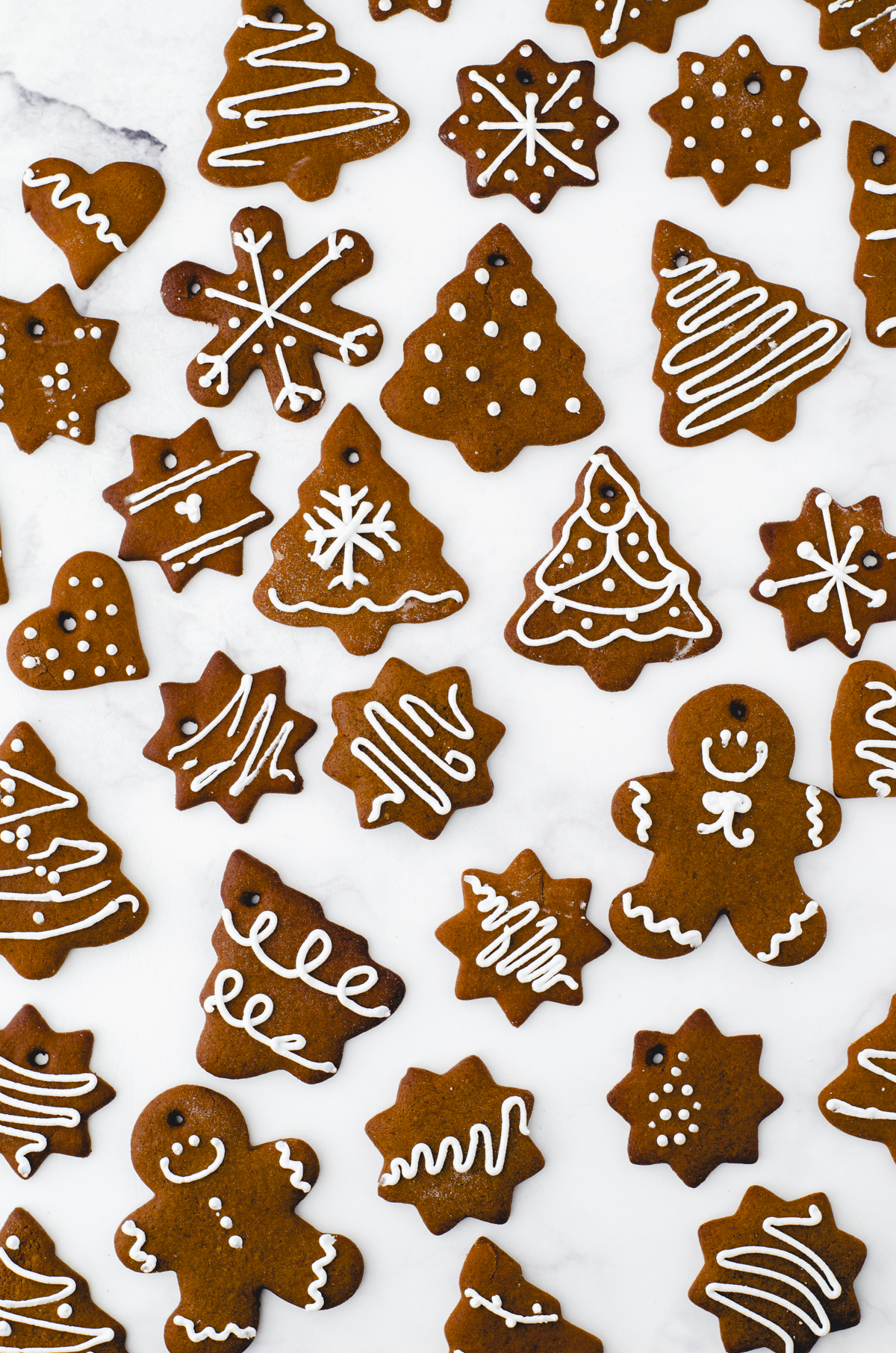 An assortment of gingerbread cookies laying on a marble surface with different designs for gingerbread cookie decorating ideas