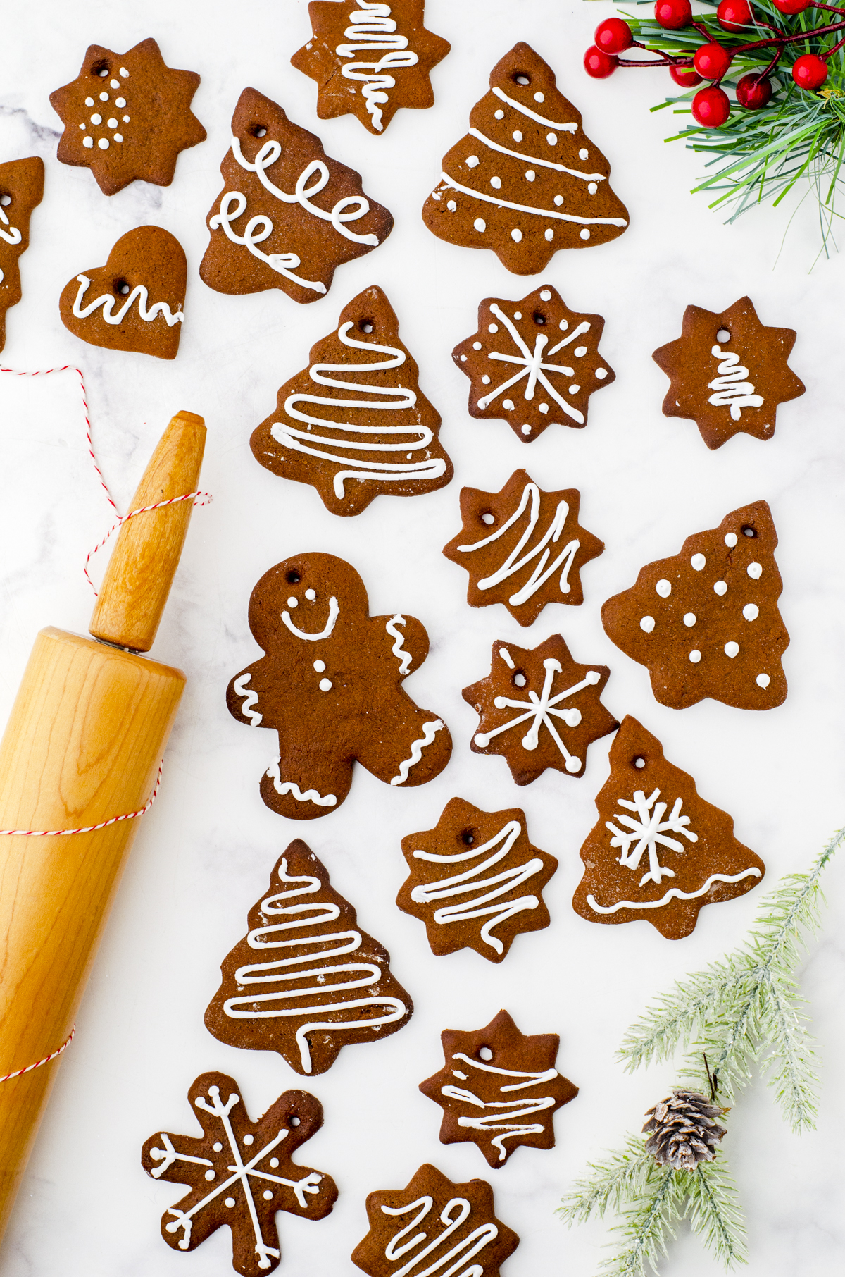 A variety of gingerbread cookies laying on a marble surface with a rolling pin beside.
