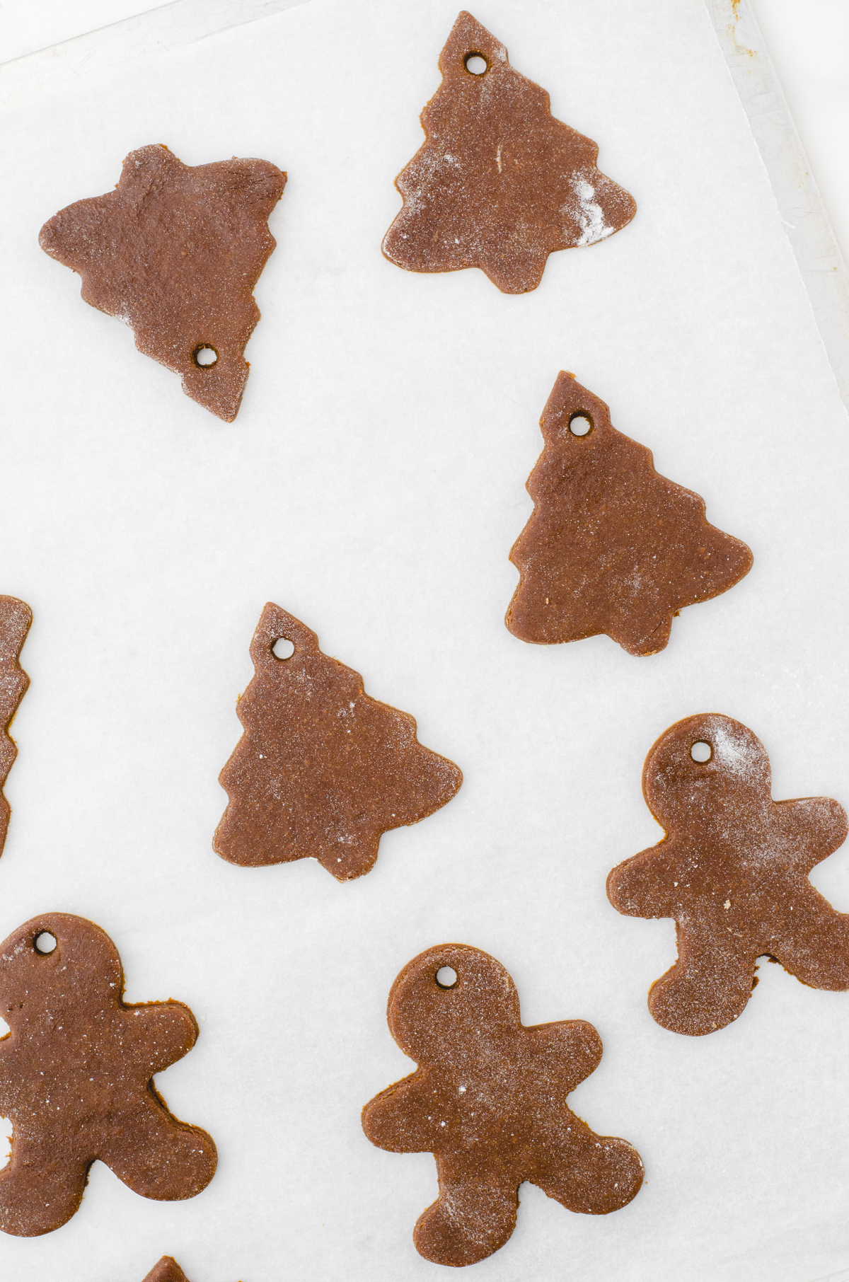 Gingerbread cookies in the shapes of christmas trees and gingerbread men on a cookie sheet ready to be baked. There is a tiny hole in the top of each one.