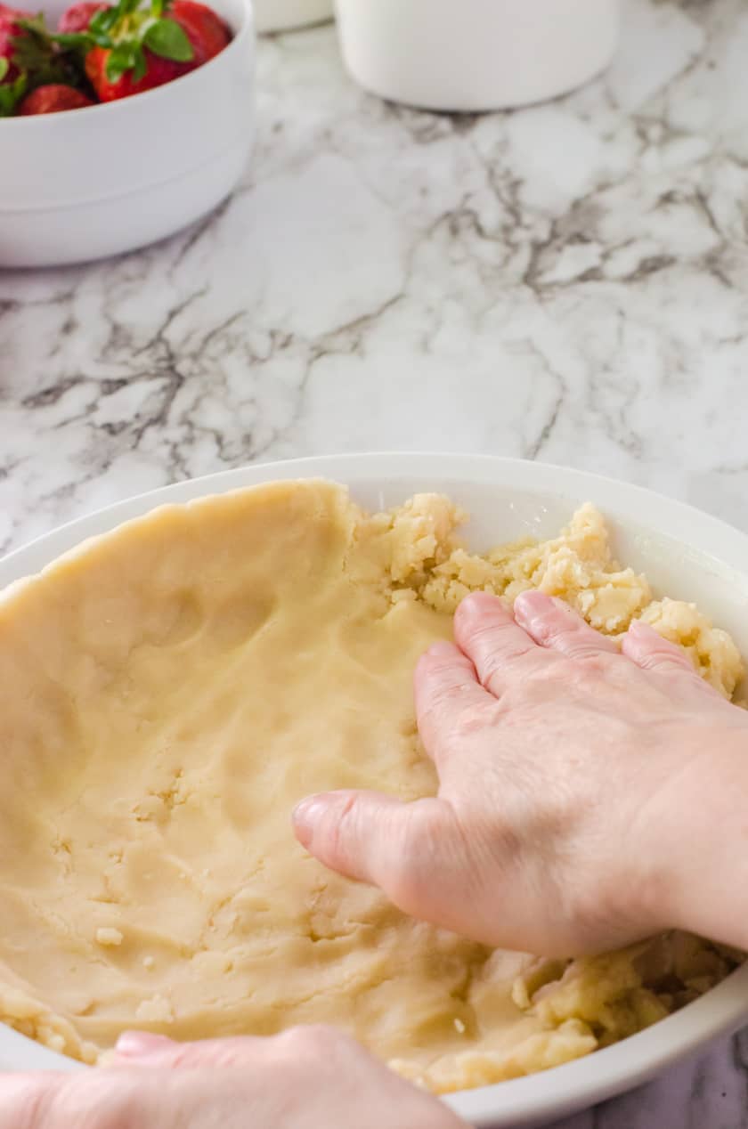 Pie crust being patted into a pie pan