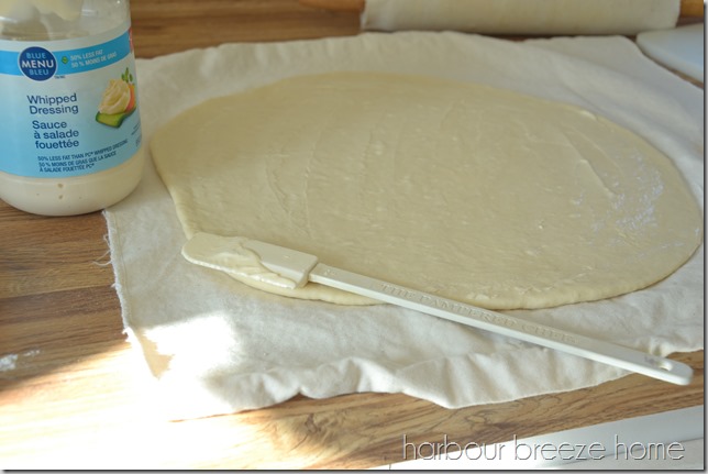 Dinner roll dough rolled out into a circle and a thin layer of miracle whip on it.