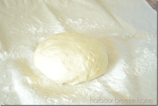 1/4 portion of dinner rolls dough formed into a round ball and sitting on a flour dusted pastry rolling cloth.
