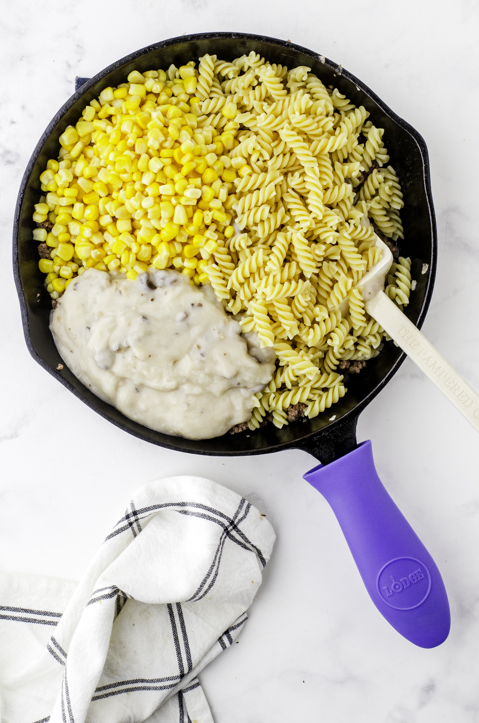 Corn, mushroom soup, and cooked pasta added to a cast iron skillet of cooked hamburger and onions for hamburger helper beef strognaff.