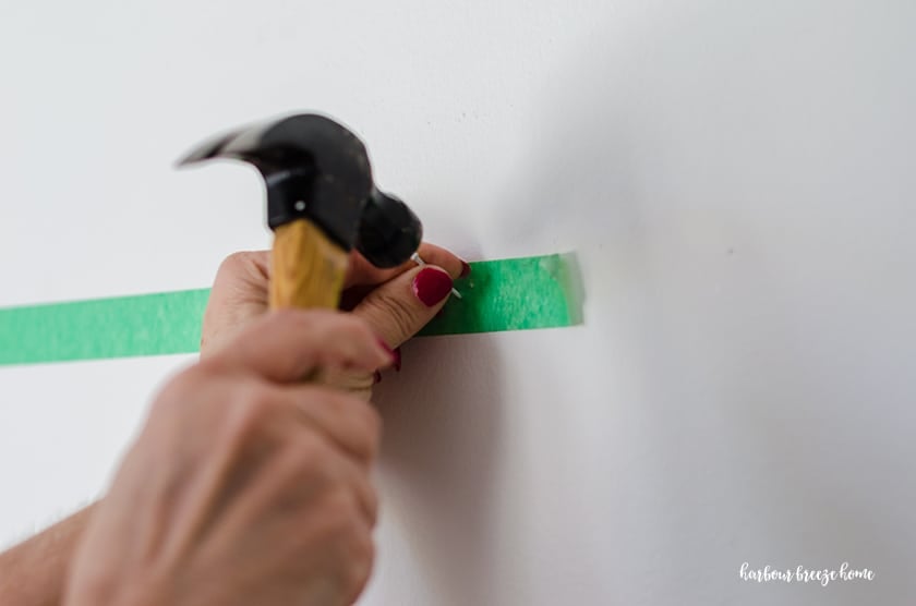 Lady hammering a nail into the wall for how to hang a picture with 2 sawtooth hangers.