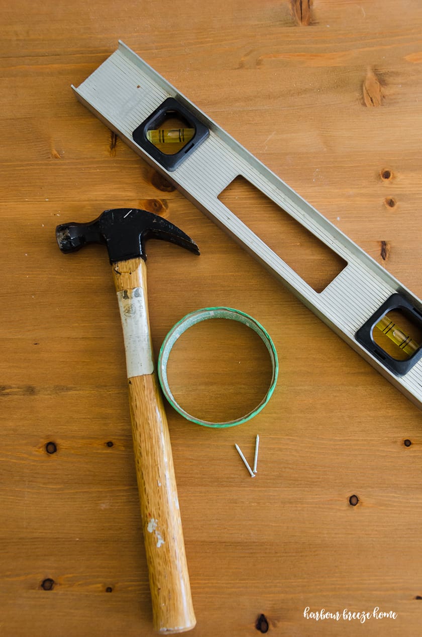 Hammer, painters tape, nails and level - supplies needed to hang a picture with 2 sawtooth hangers in drywall.