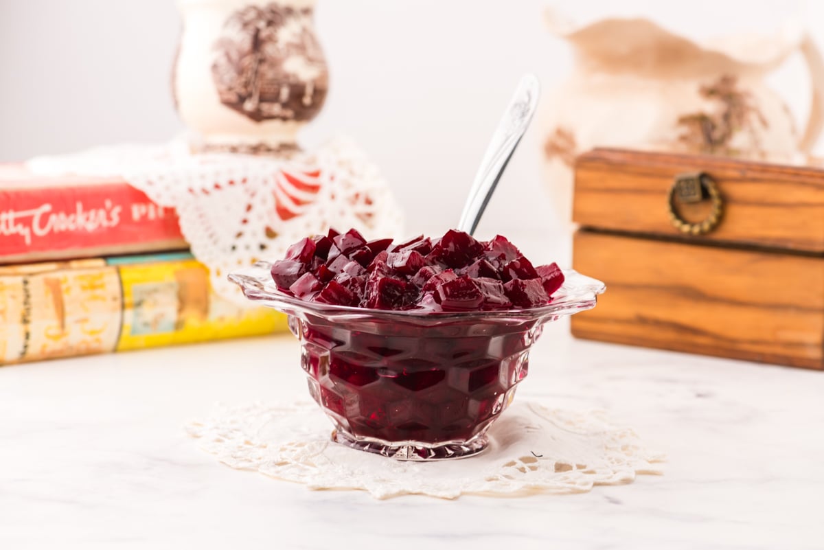 A bowl of harvard beets on a crocheted doily with antique cookbooks and an antique recipe box behind it.