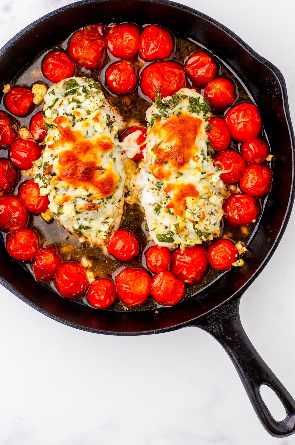 Spinach & feta stuffed hasselback chicken baked over tomatoes in a cast iron pan