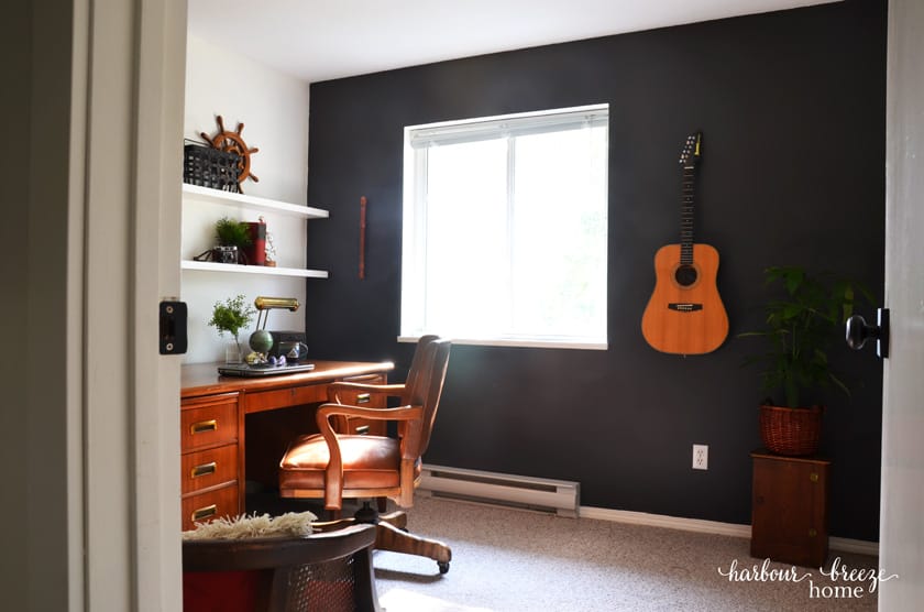 a masculine work from home office with a dark accent wall and wooden desk